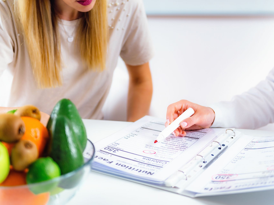 Vers la page Suivi personnalisé Une personne consulte quelqu'un au sujet d'un plan nutritionnel, en montrant ses notes.