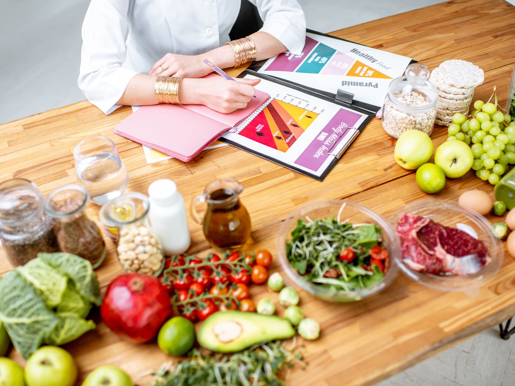 Vers la page Nutritionniste/Diététicienne Une personne écrit dans un carnet, entourée d'aliments sains disposés sur une table.
