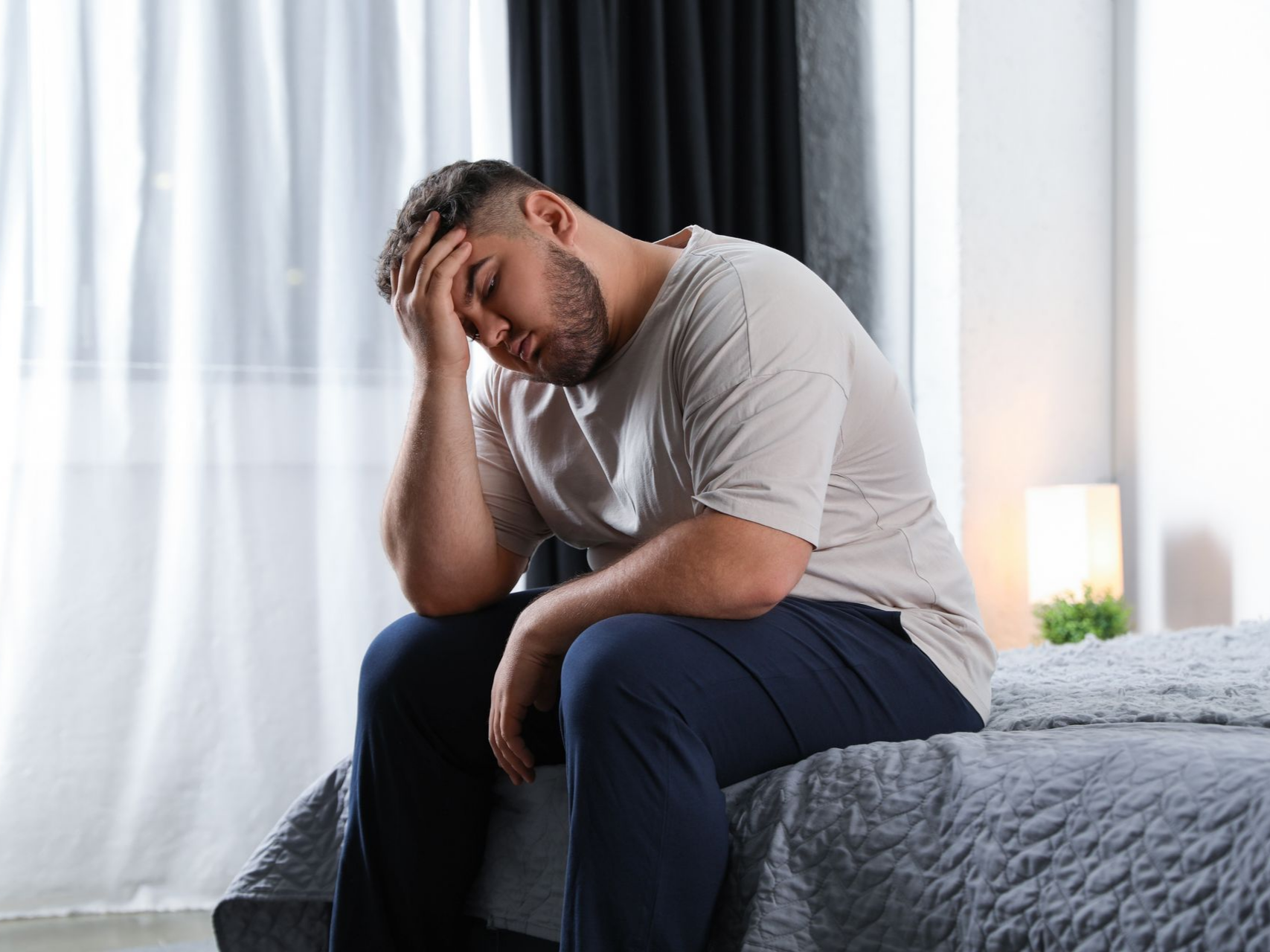 Vers la page Pour qui ? Un homme assis sur un lit, la tête dans les mains dans sa chambre.