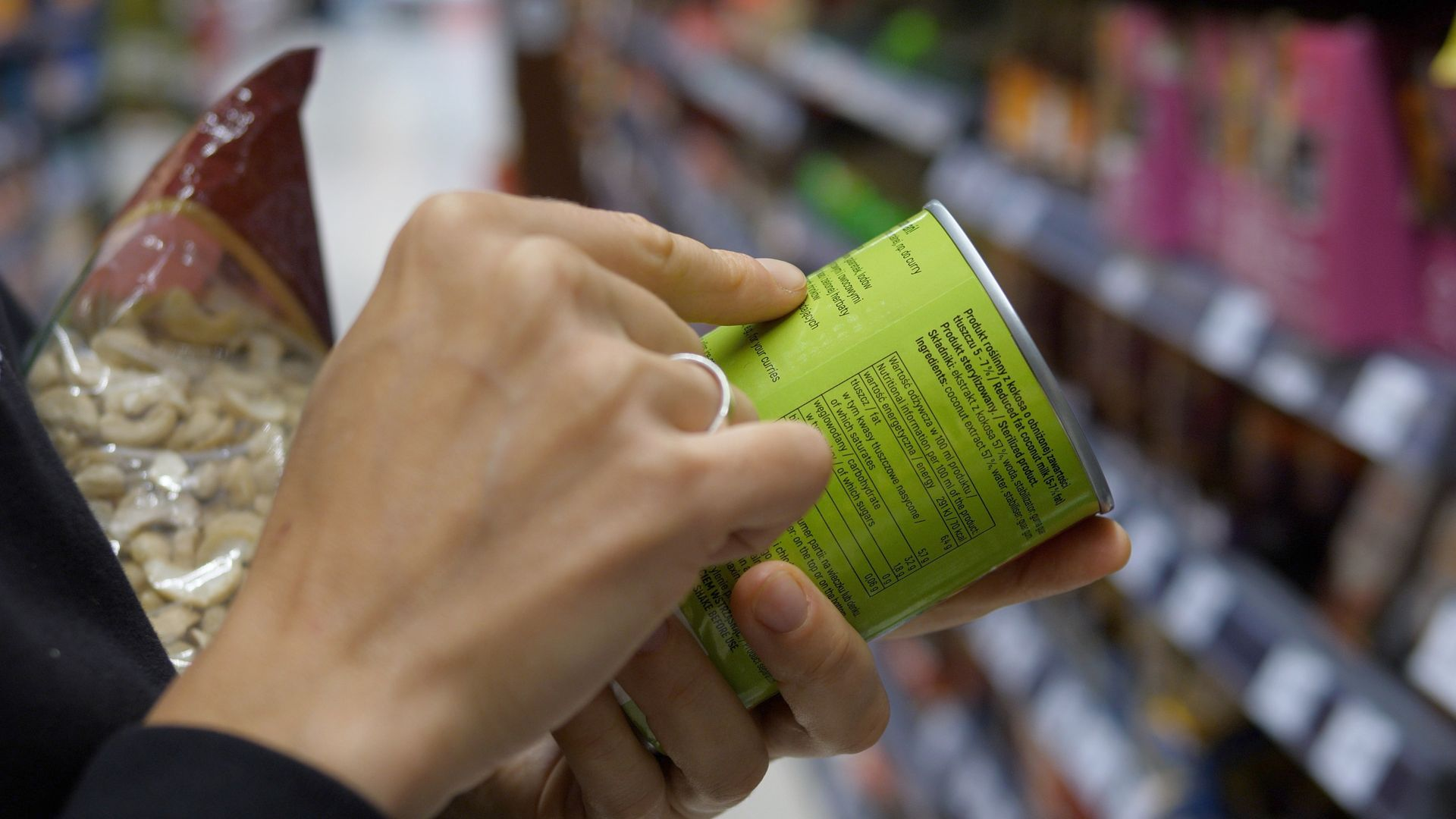 Une personne tenant une conserve verte, en train de lire l'étiquette dans un rayon de supermarché.