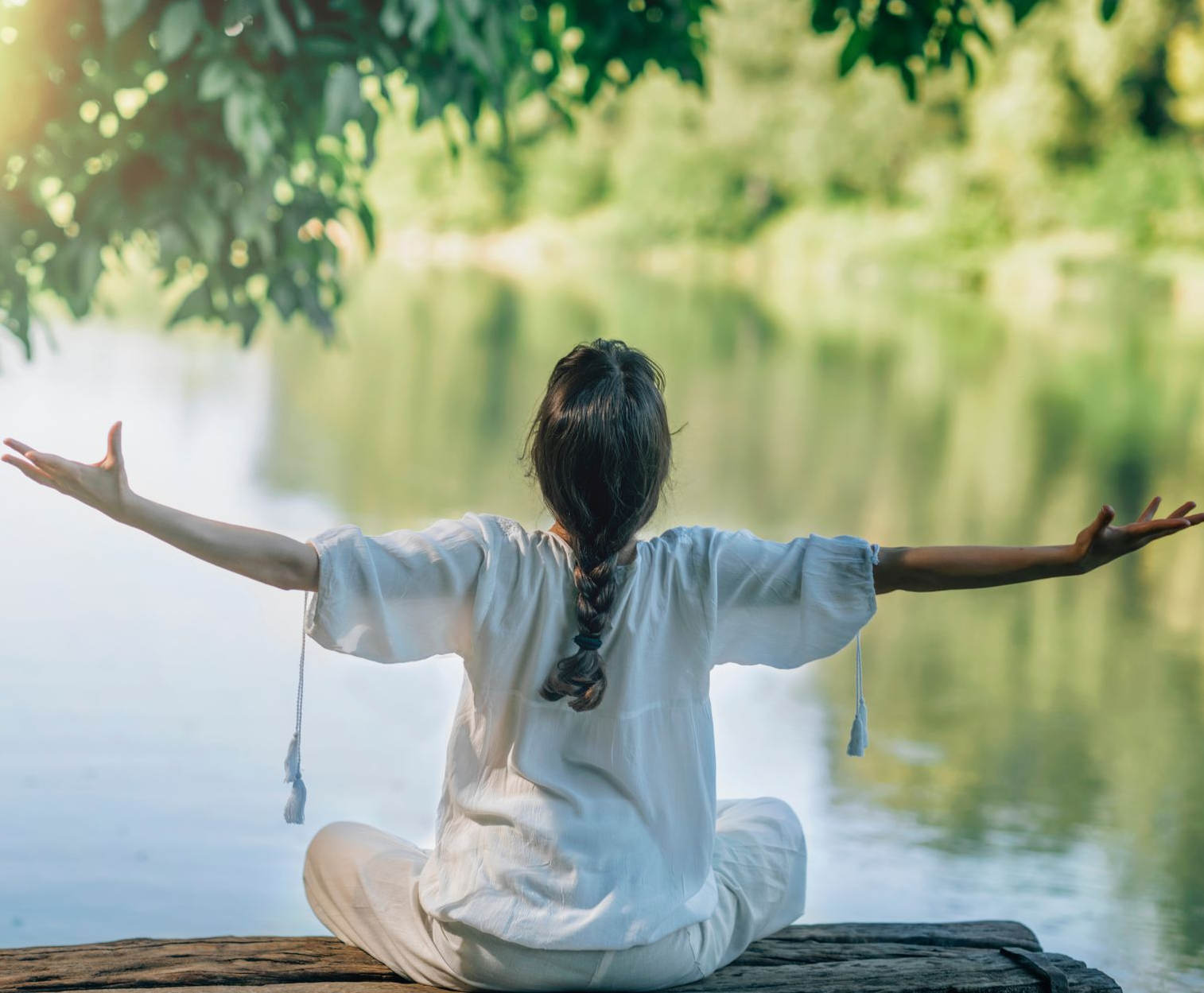 Femme assise en lotus, les bras étendus, près d'un lac.