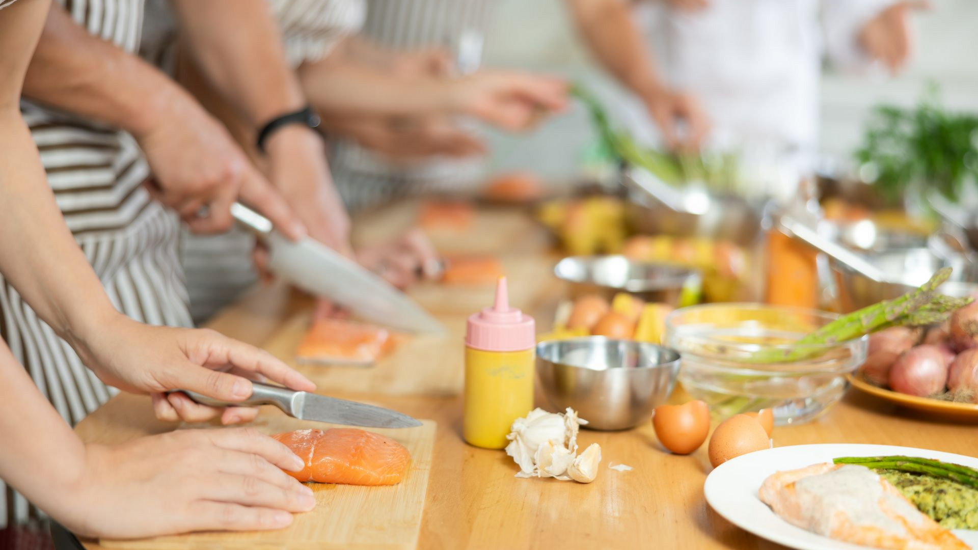 Des personnes participent à un cours de cuisine en découpant du saumon sur des planches à découper en bois.