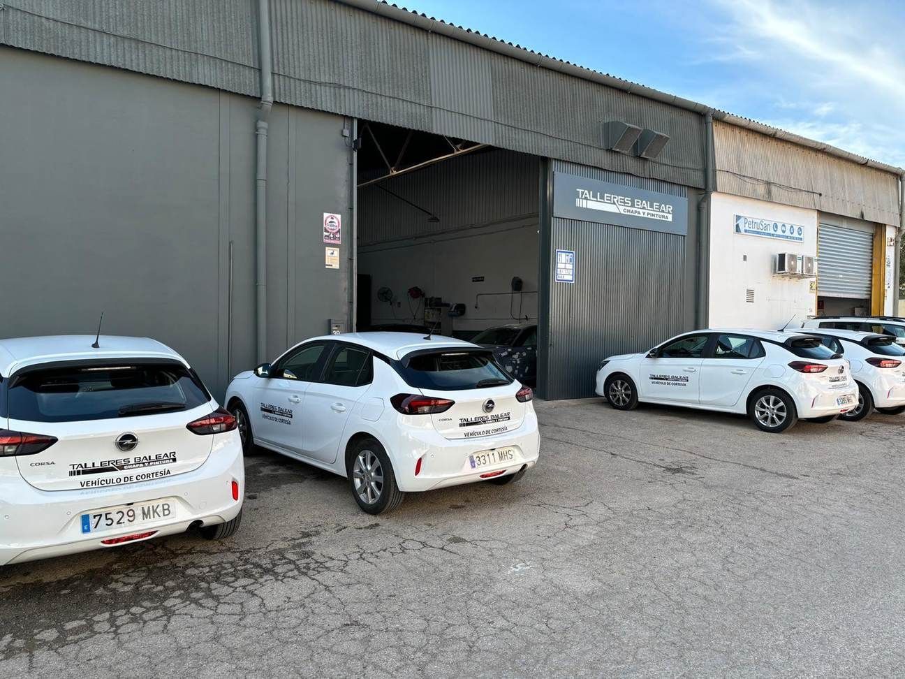 Varios coches blancos aparcados frente a un garaje industrial abierto, con un coche dentro.