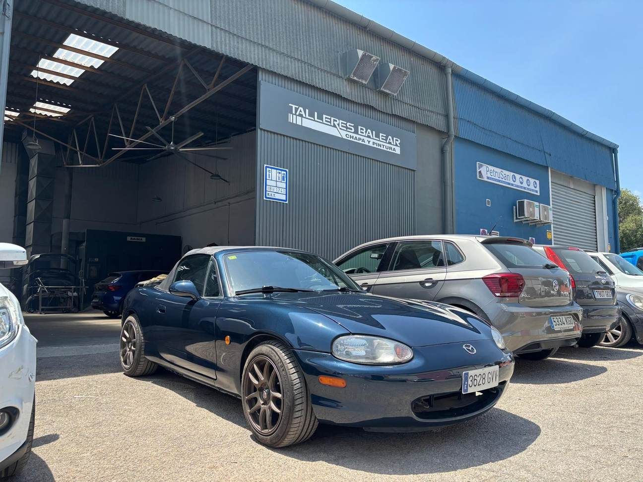 Coche deportivo azul aparcado frente a un taller mecánico, con otros coches cerca