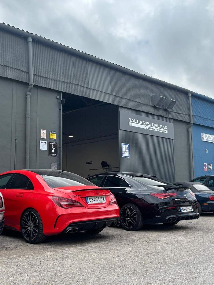 Tres coches aparcados frente a un garaje industrial, entre ellos un SUV rojo y un sedán negro, bajo un cielo nublado