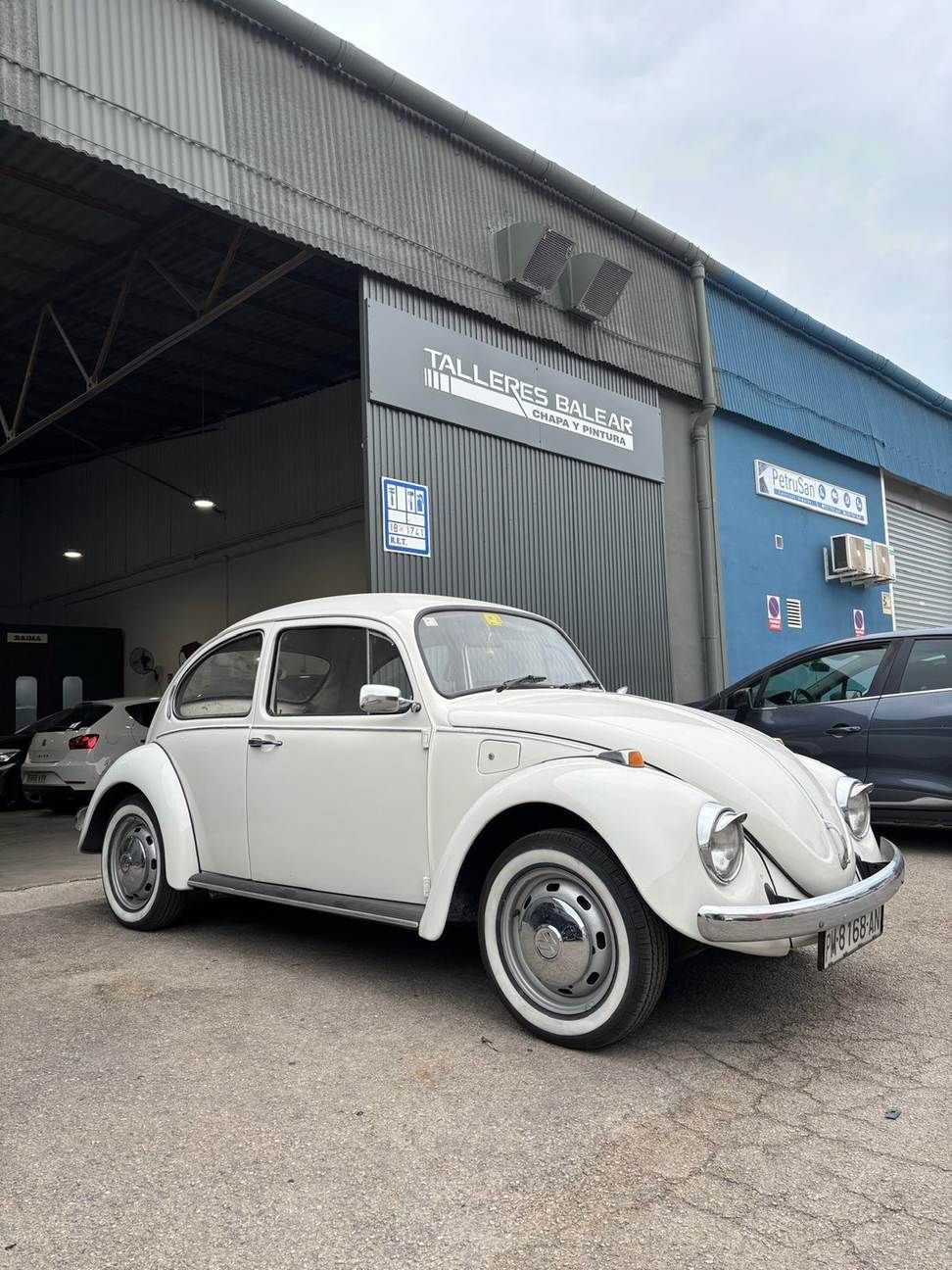 Volkswagen Beetle blanco de época estacionado frente a un garaje azul
