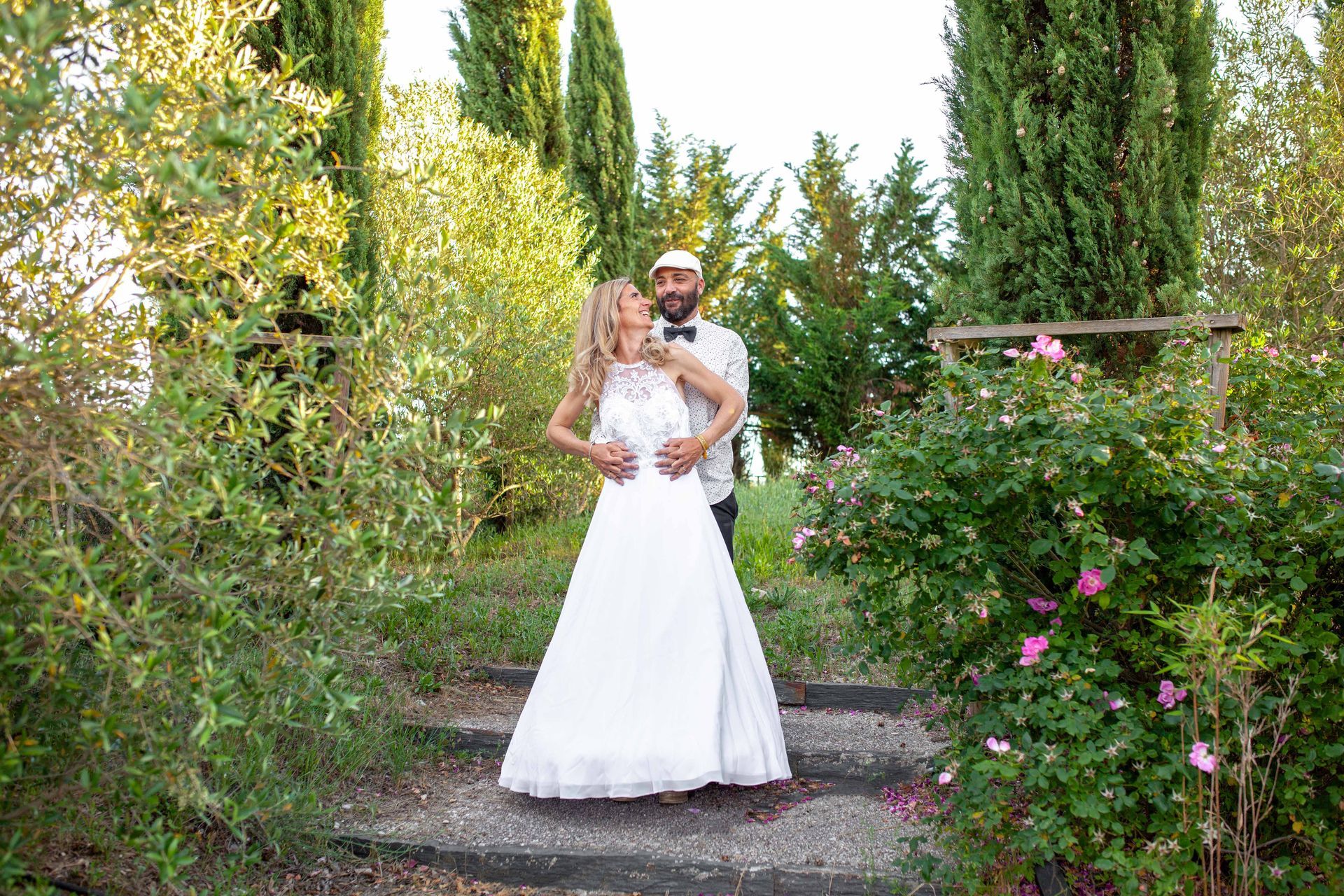 Les mariés s'embrassent sur les marches d'un jardin. La mariée porte une robe blanche.