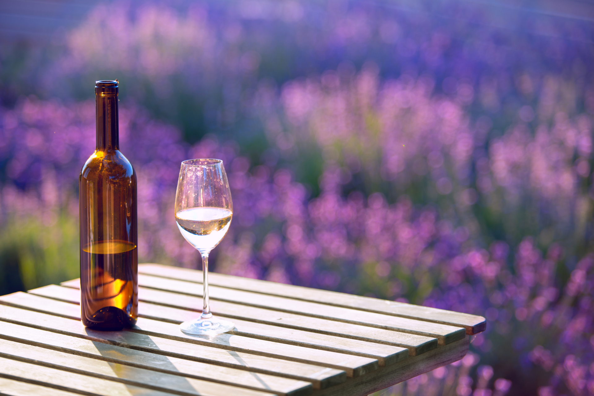 Bouteille de vin et verre sur une table en bois, avec un champ de lavande en arrière-plan.