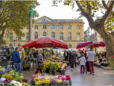 Marché aux fleurs sur une place européenne avec des gens parcourant des fleurs colorées.
