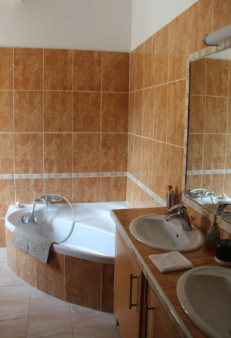 Salle de bain avec murs carrelés orange, baignoire blanche et double vasque.