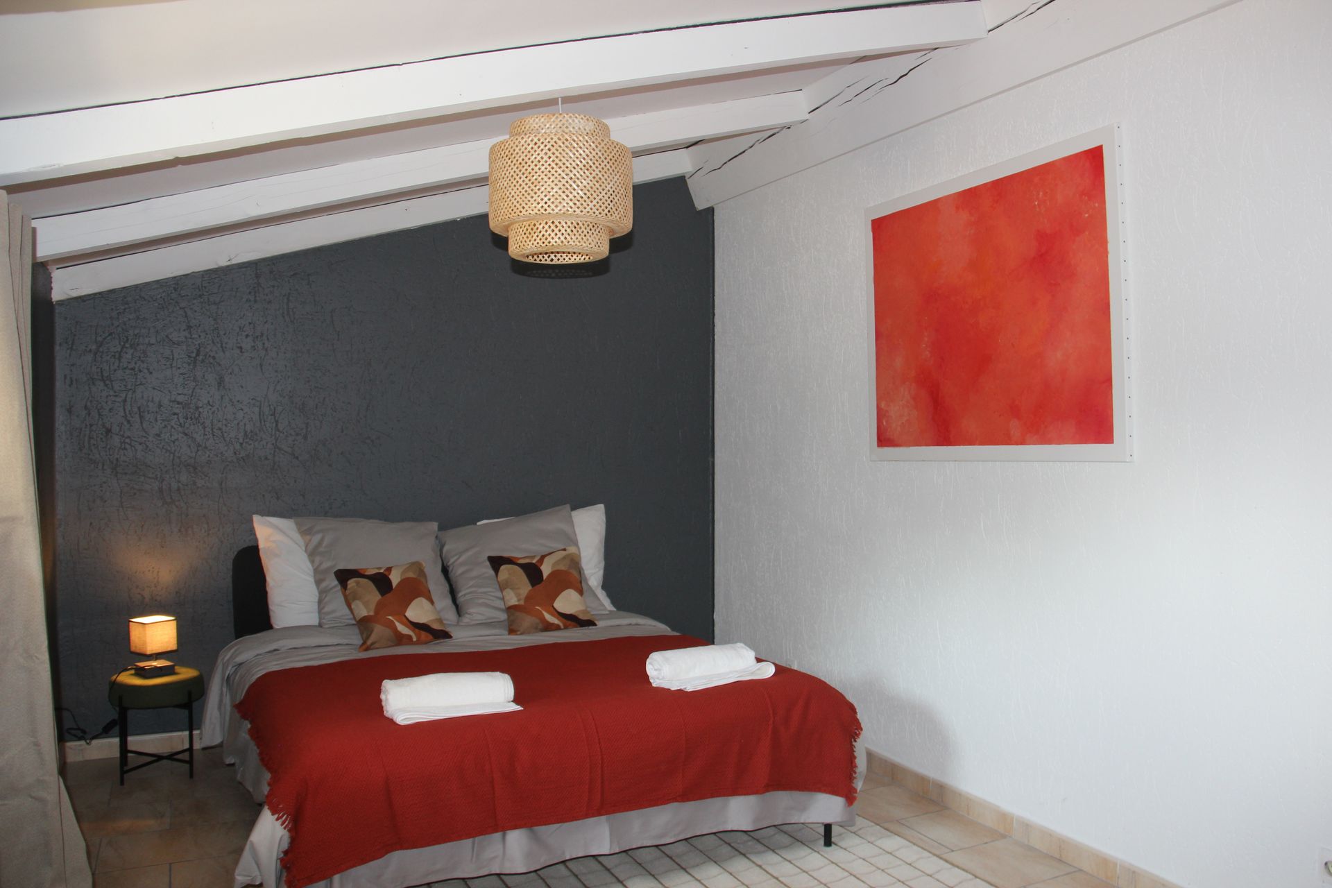 Chambre avec un mur gris foncé, un lit avec une couverture rouge, des œuvres d'art orange et une suspension tissée.