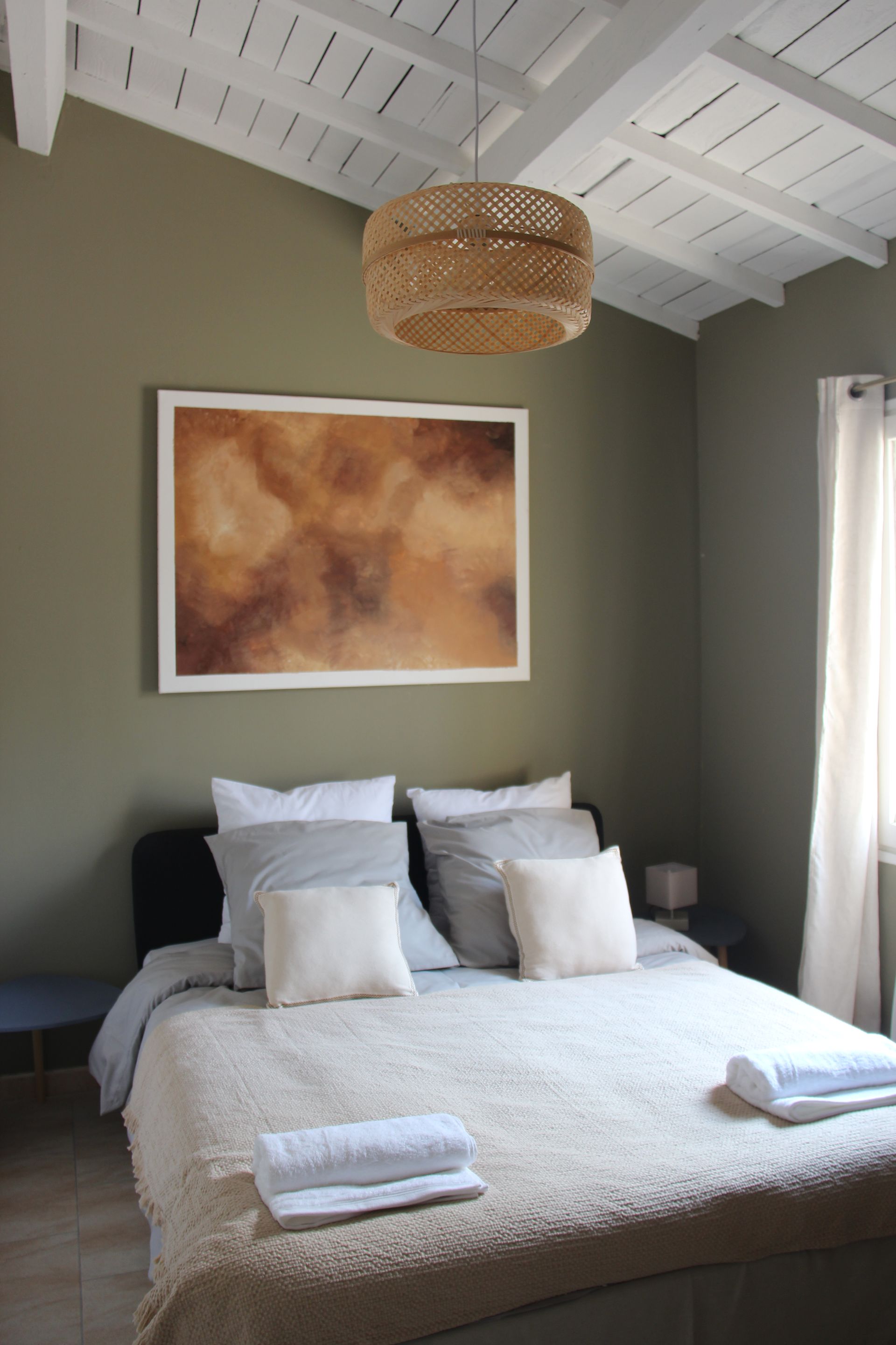 Chambre avec lit, œuvres d'art et abat-jour tissé ; murs vert olive et plafond blanc.