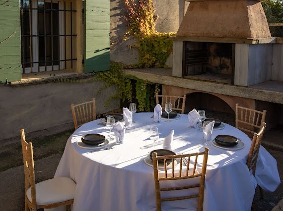 Terrasse extérieure avec une table en béton, des chaises tressées et un barbecue en pierre intégré sous un ciel bleu.