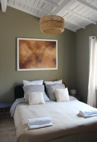 Chambre avec lit, œuvres d'art et abat-jour tissé. Murs vert olive, plafond blanc.