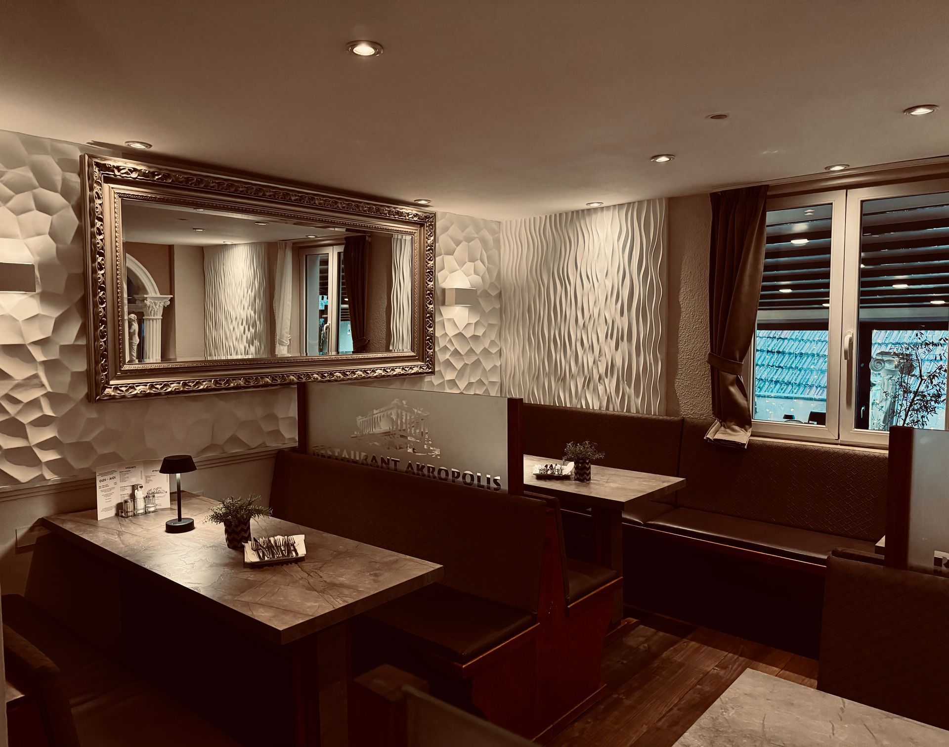 Innenraum einer Restaurantkabine mit braunen Sitzgelegenheiten, strukturierten Wänden und einem großen Spiegel.