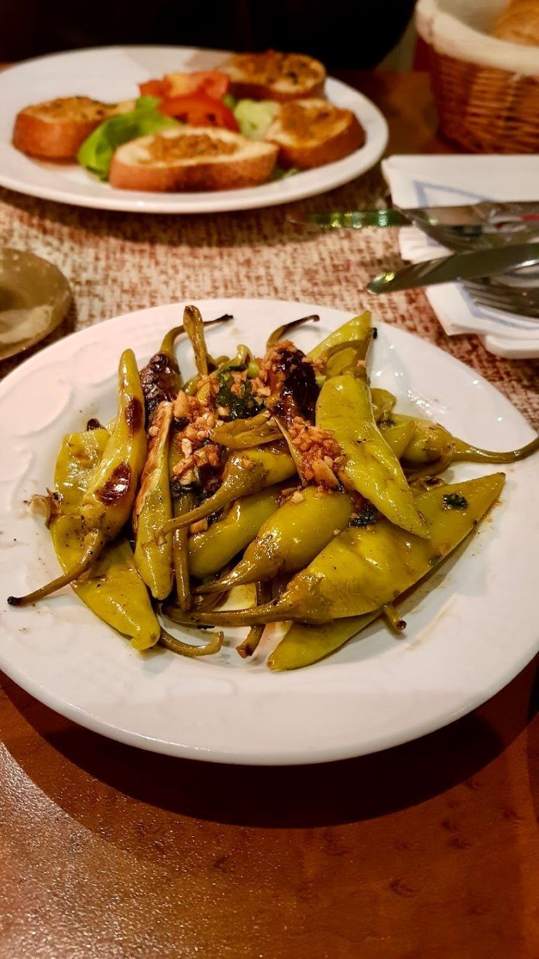 Teller mit gerösteten grünen Paprikaschoten, gewürzt; andere Gerichte auf dem Tisch.