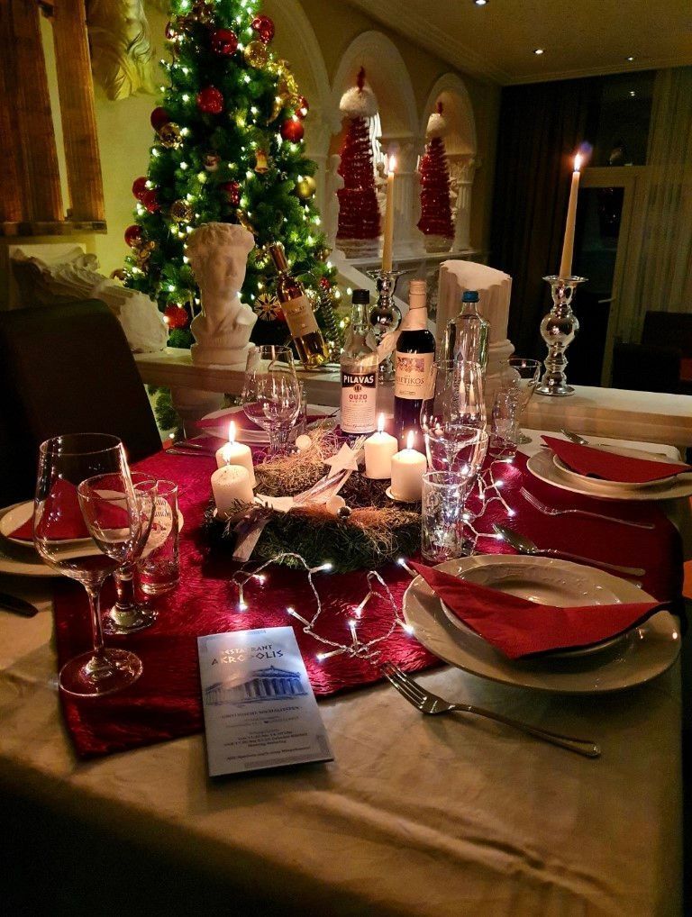 Festliche Weihnachtstafel mit roten Akzenten, Kerzen und einem geschmückten Baum im Hintergrund.