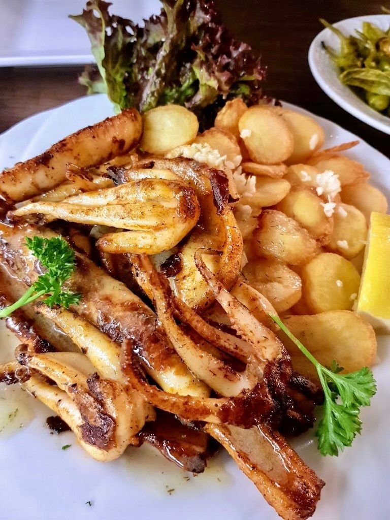 Teller mit gegrilltem Tintenfisch, Kartoffeln, Gemüse und Zitrone.