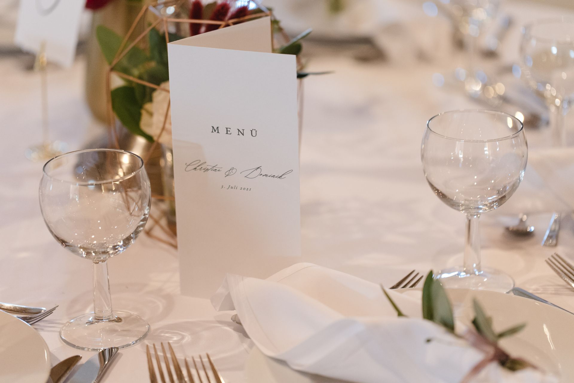 Ein für einen Hochzeitsempfang gedeckter Tisch mit Menü und Weingläsern