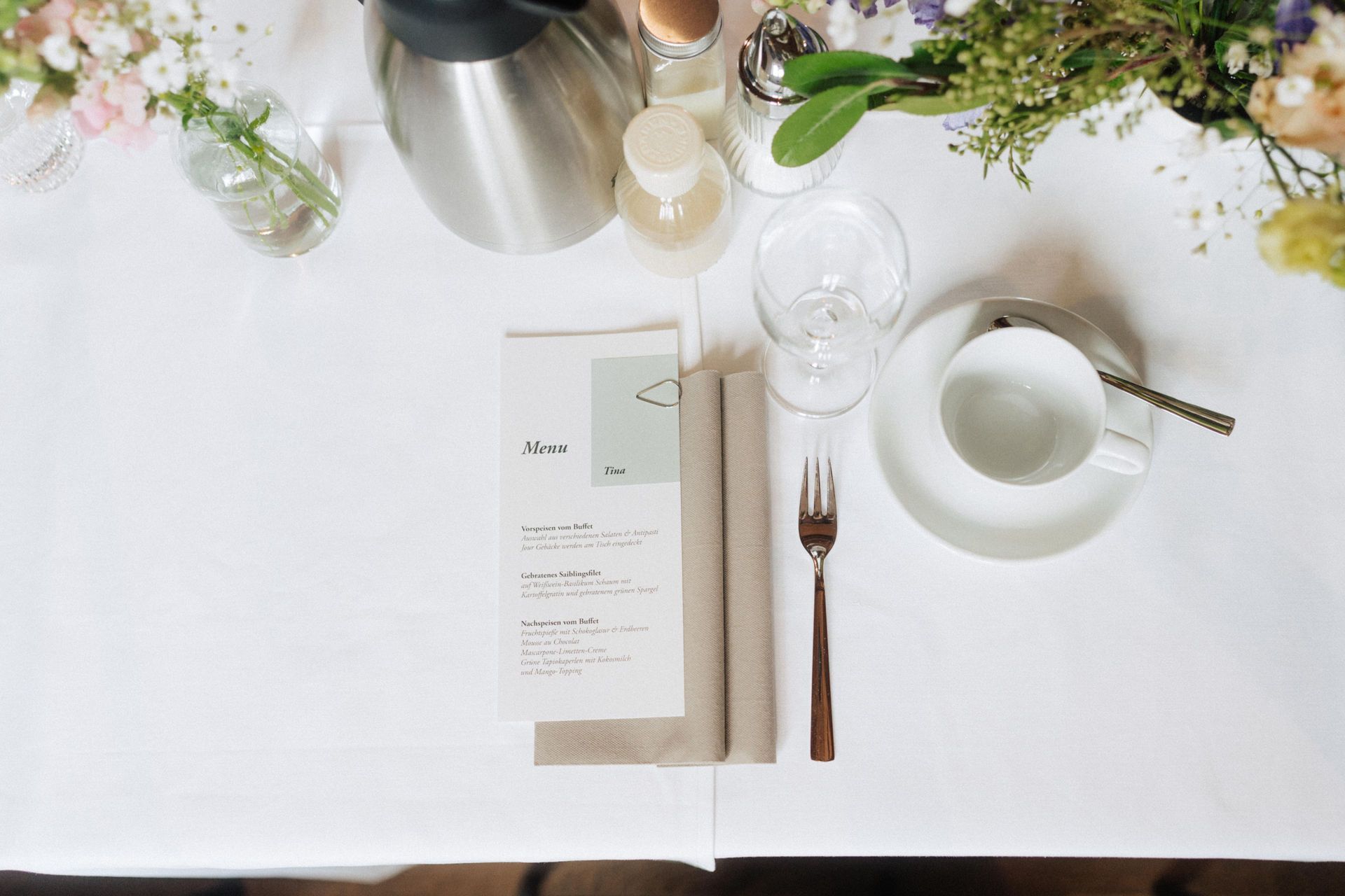 Ein Tisch mit einer Speisekarte, Besteck, Tassen und Blumen darauf