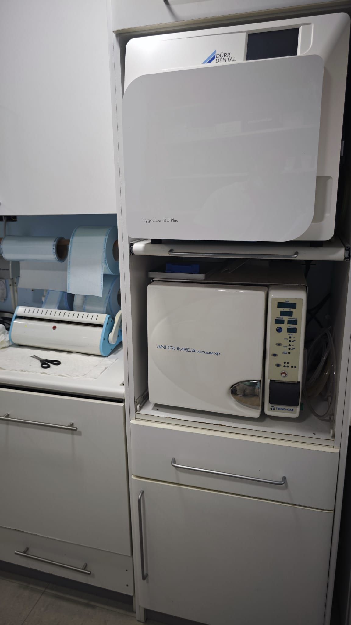 Sobre una encimera hay equipo de laboratorio, con instrumental médico apilado y un armario beige debajo.