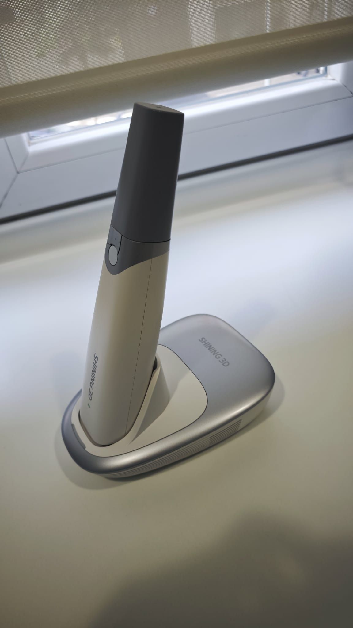 Teléfono inalámbrico en blanco y negro sobre una base de carga junto a una ventana.