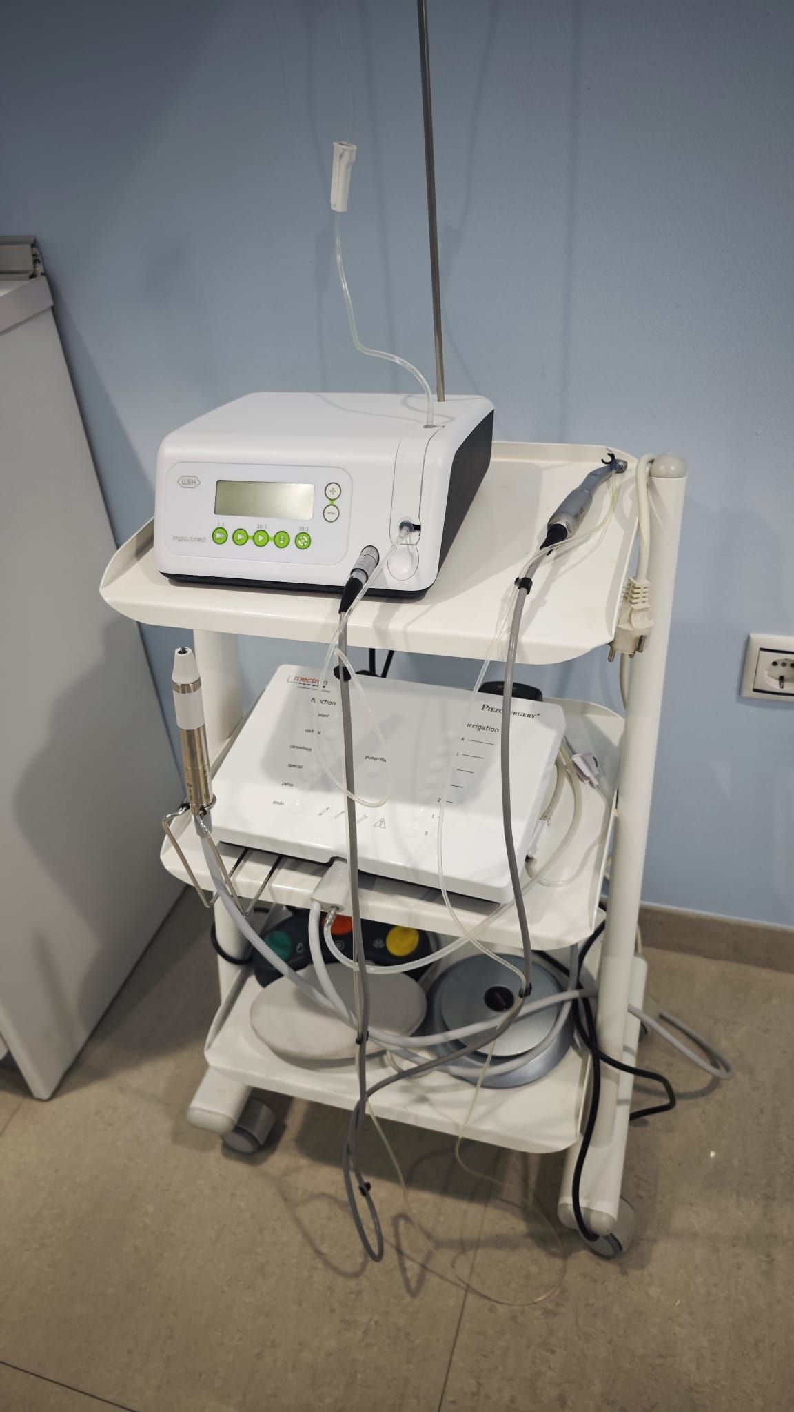 Carro de instrumental médico con un dispositivo blanco y cables en una sala clínica.