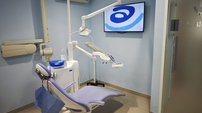 Sala de examen dental con sillón reclinable, luces de techo y monitor montado en la pared.