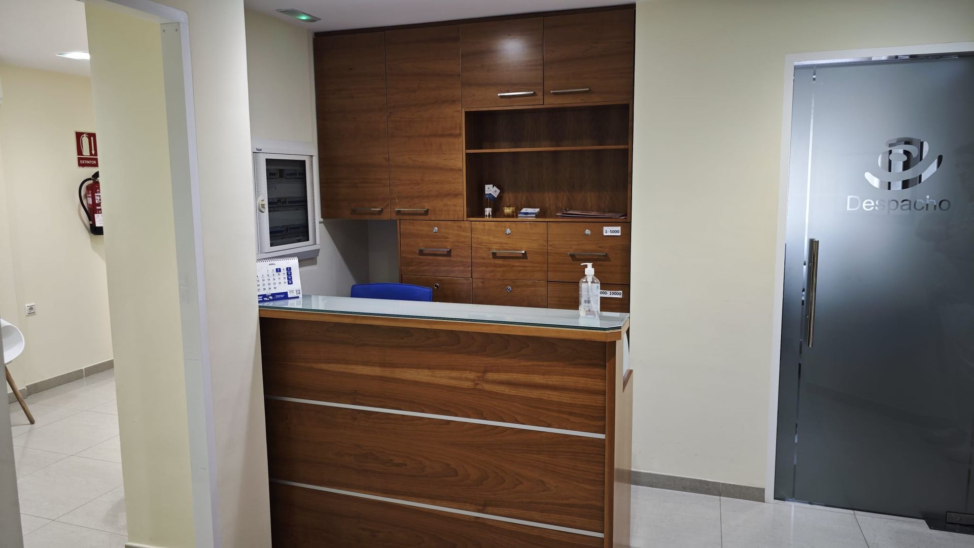 Mostrador de recepción en un vestíbulo con paneles de madera, paredes blancas y una puerta de vidrio esmerilado.