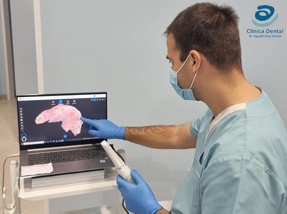 Consultorio dental con sillón dental azul, lámpara de exploración, armarios y persianas en las ventanas.