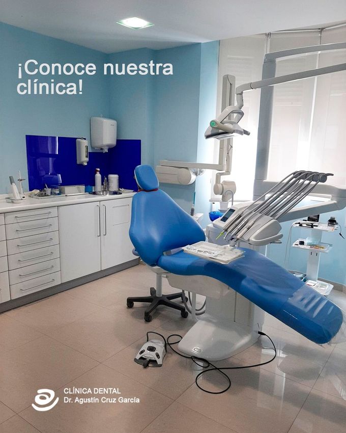 Sala de examen dental con sillón, luz cenital, armarios y equipo médico en una clínica azul y blanca.