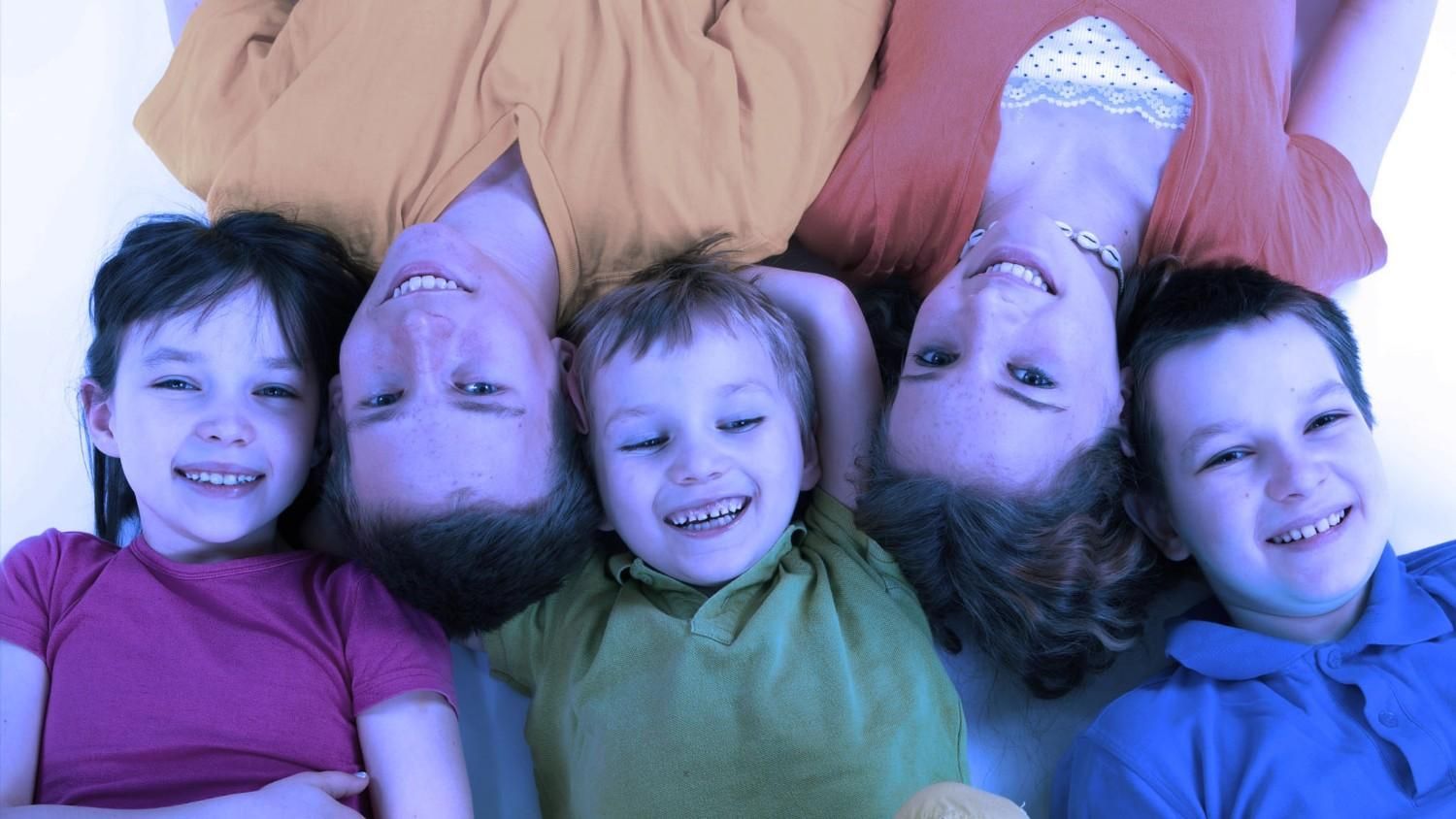 Cuatro niños tumbados uno al lado del otro, sonriendo a la cámara con coloridos jerséis.