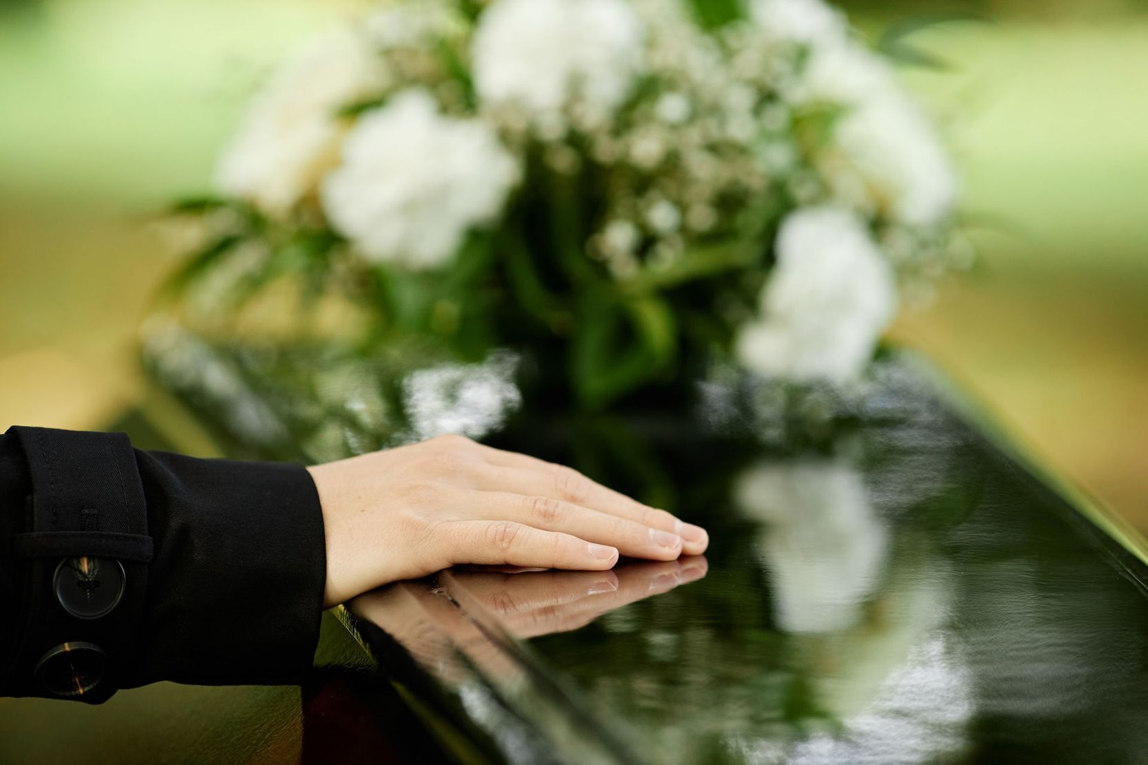 Main d'une femme sur un cercueil noir surmonté de fleurs