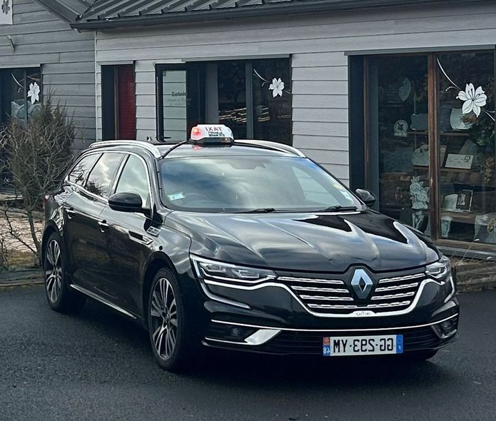 Un taxi Renault noir est stationné dans la rue, devant un immeuble.