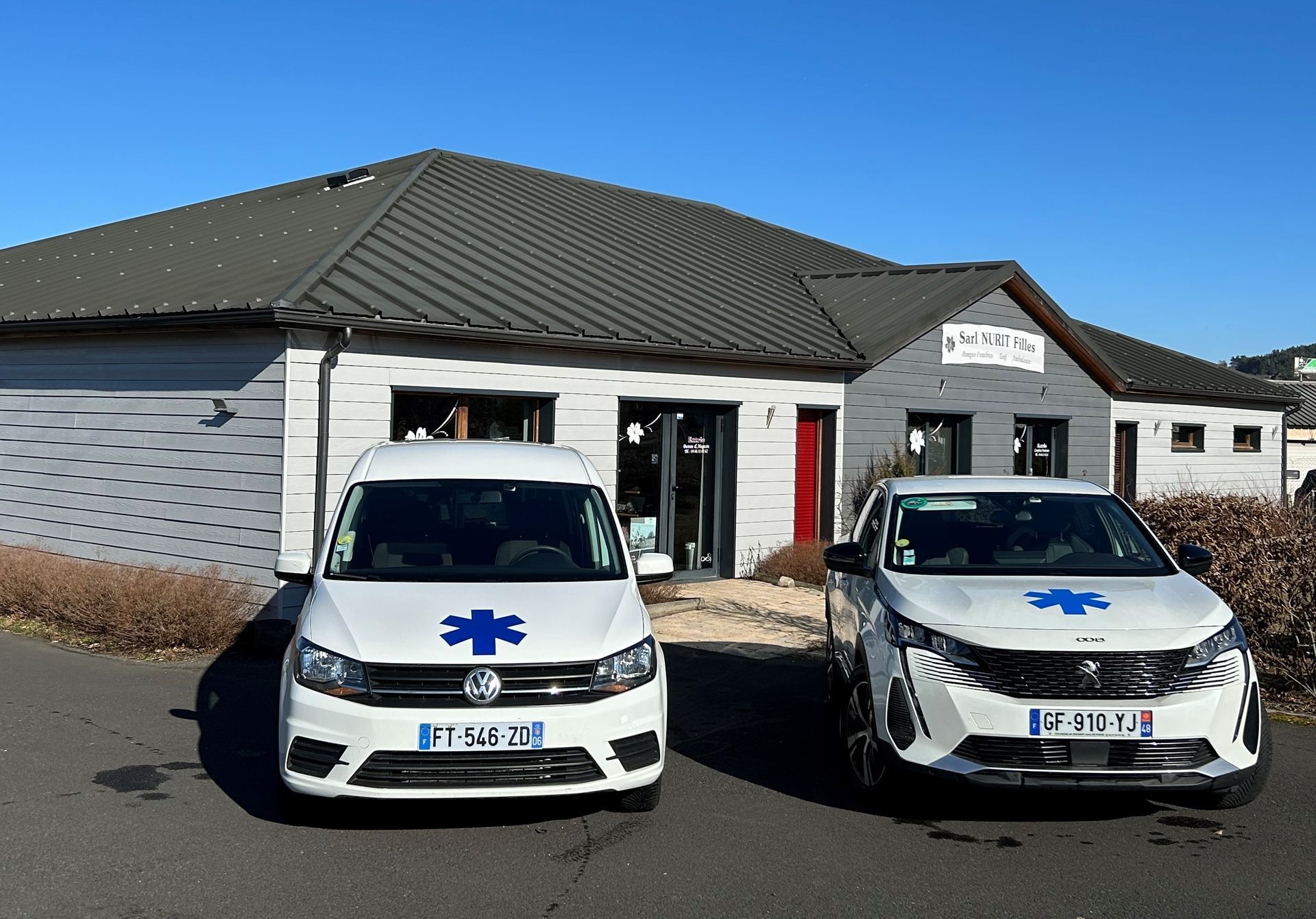 Deux ambulances blanches étaient garées devant un bâtiment au toit sombre et à la façade en briques.