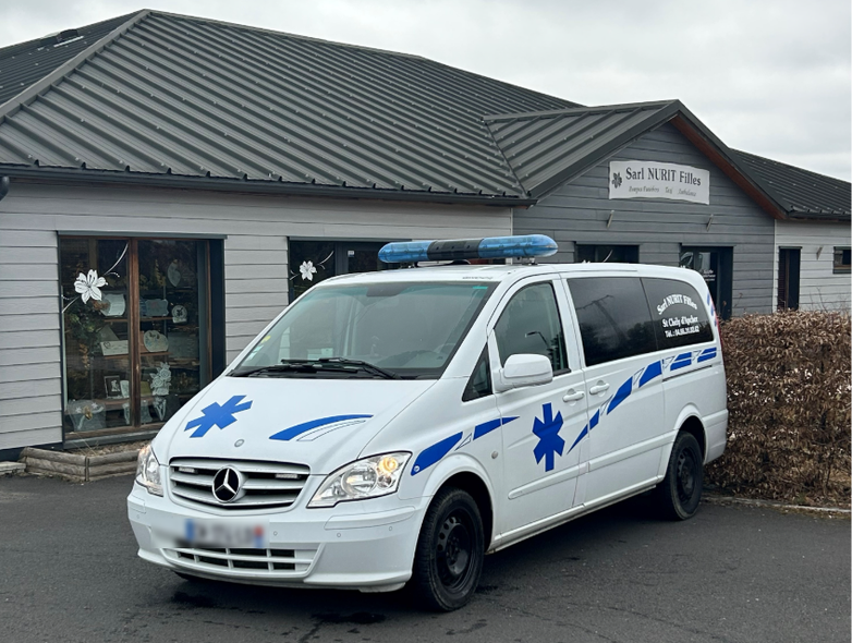 Une ambulance blanche avec des marquages ​​d'urgence bleus est garée devant un bâtiment.