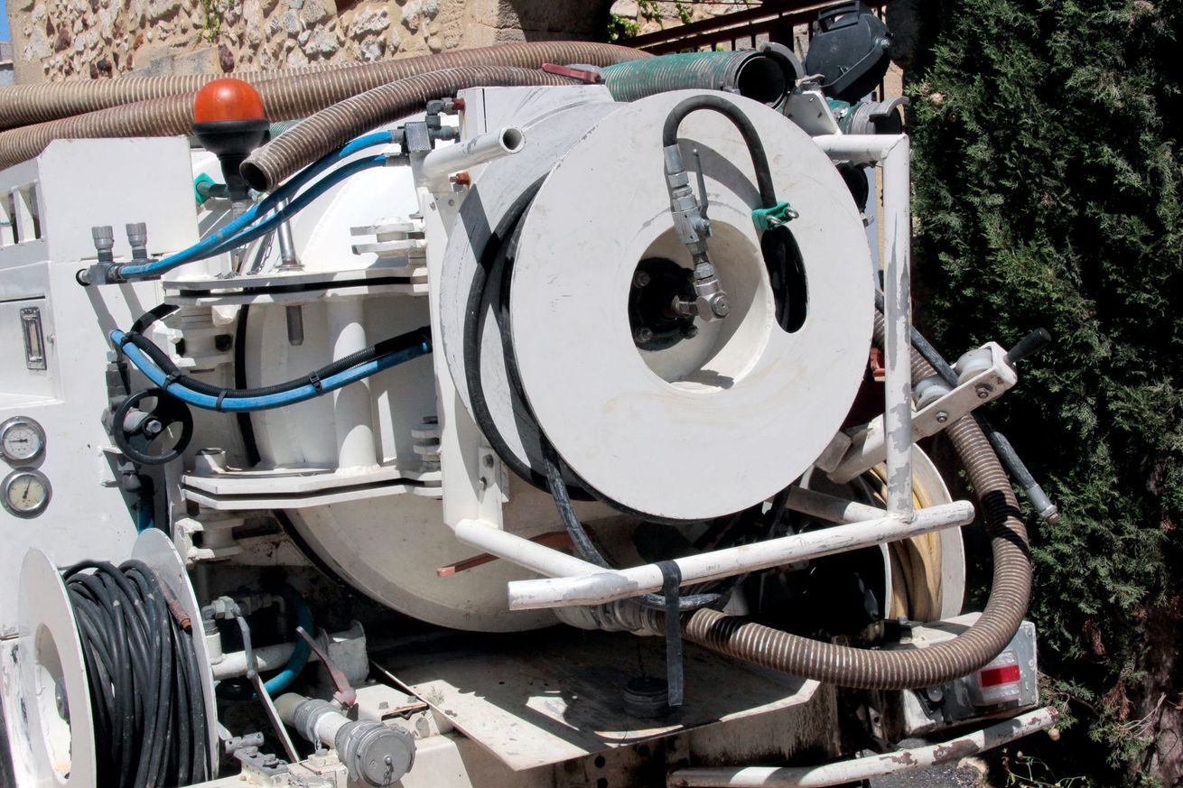 Machine industrielle blanche avec tuyaux et grande bobine circulaire à l'extérieur, près des arbres et des rochers.