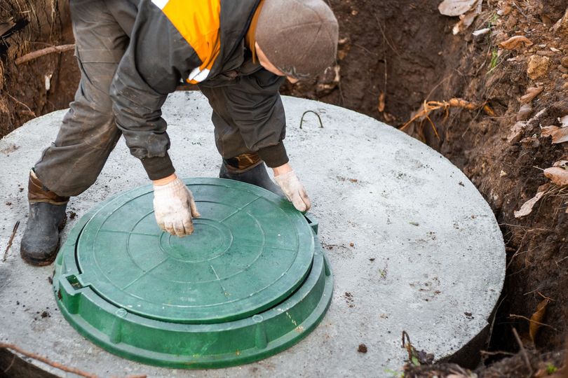 Un ouvrier ouvre une plaque d'égout verte dans un regard de visite en béton.