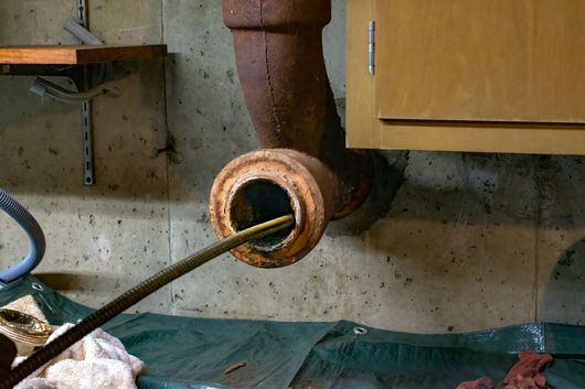 Un tuyau rouillé sort d'un mur en béton, une longue tige y est insérée.