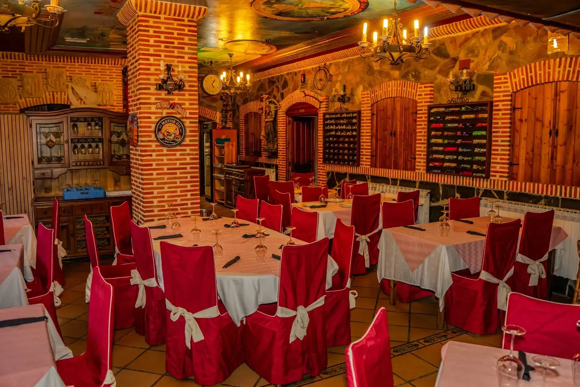 Elegante comedor de restaurante con fundas rojas en las sillas, manteles blancos y una cálida iluminación dorada.