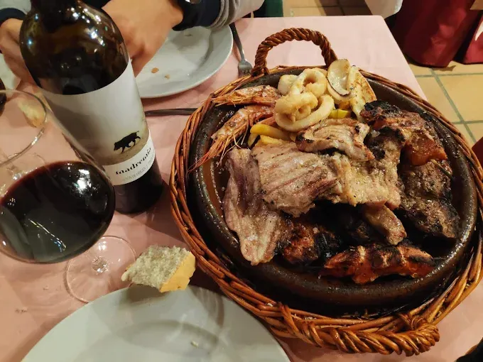Vino y una cesta de carne a la parrilla y patatas fritas en la mesa de un restaurante.