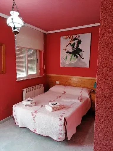 Dormitorio rosa con cama, cuadro floral en la pared, persianas y radiador blanco.