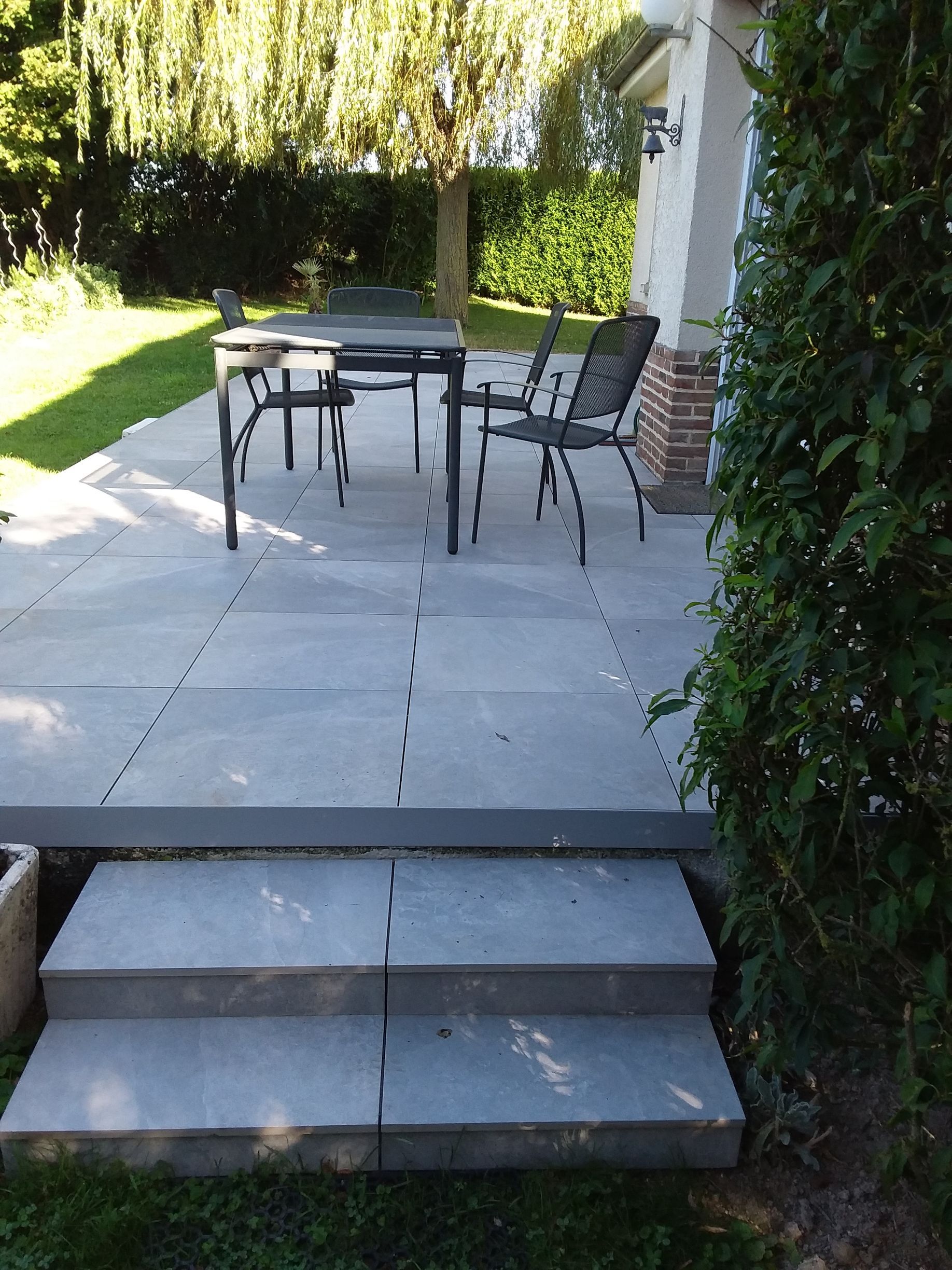Une terrasse carrelée avec une table et deux chaises.
