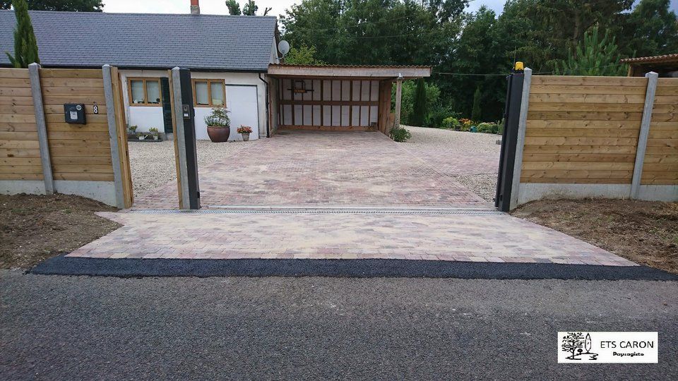 Portail en bois ouvert donnant sur une allée de gravier et l'entrée d'une maison moderne.
