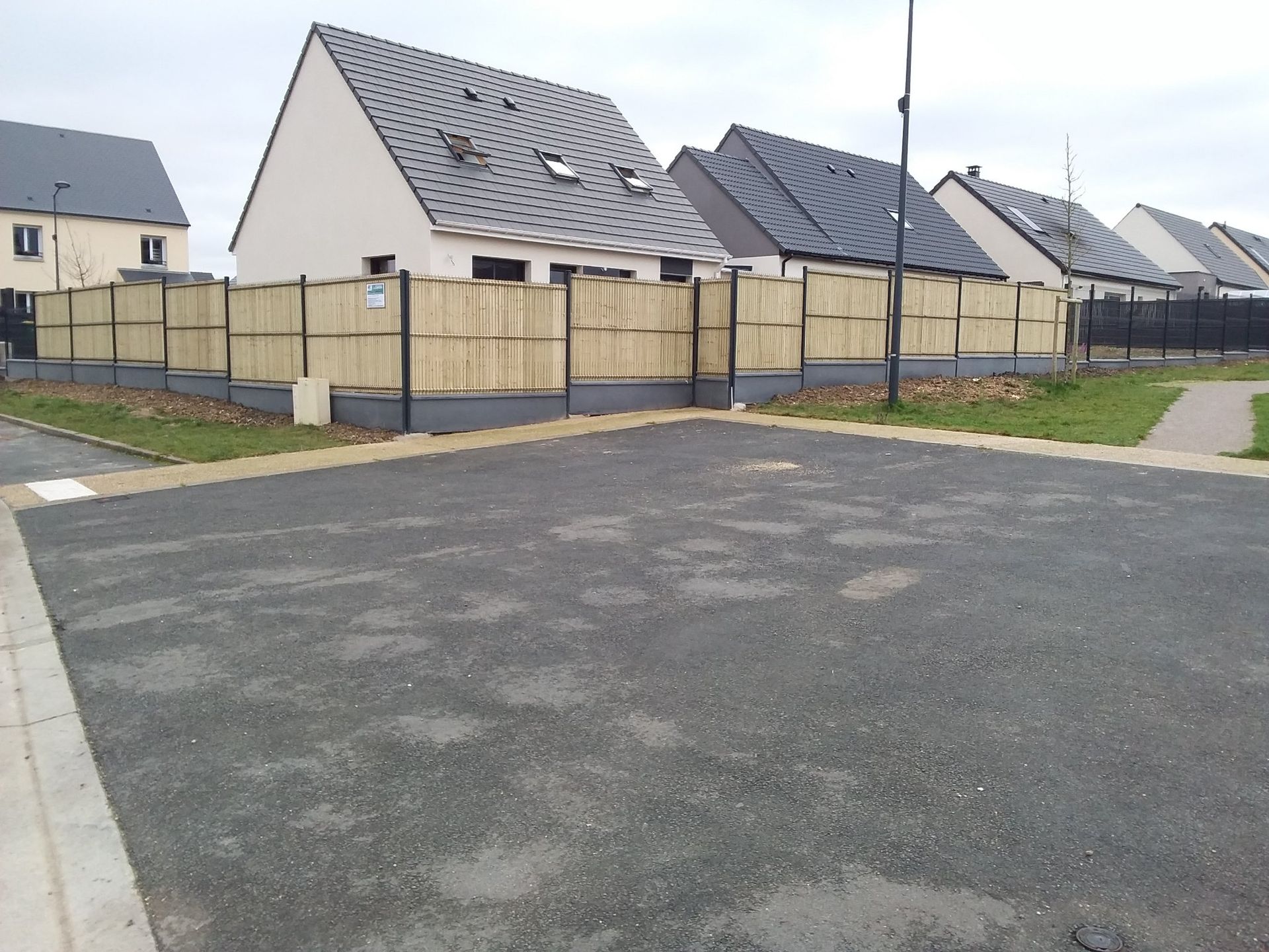 Rue résidentielle avec des maisons neuves, des cours clôturées et une route goudronnée vide.