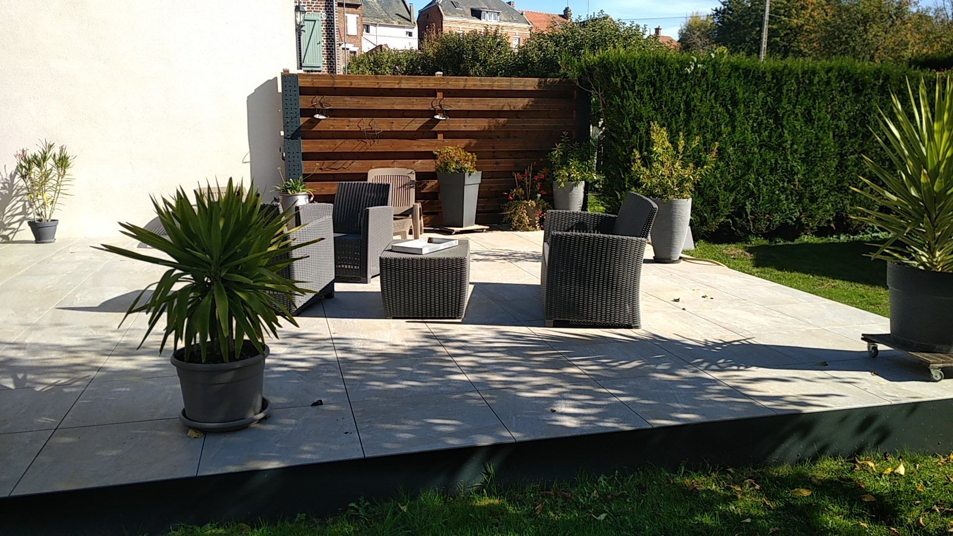 Patio moderne avec banc en bois, sièges en osier, jardinières et plantes en pot baigné de soleil.