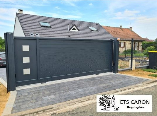 Garage gris moderne avec puits de lumière et allée pavée dans un quartier résidentiel.