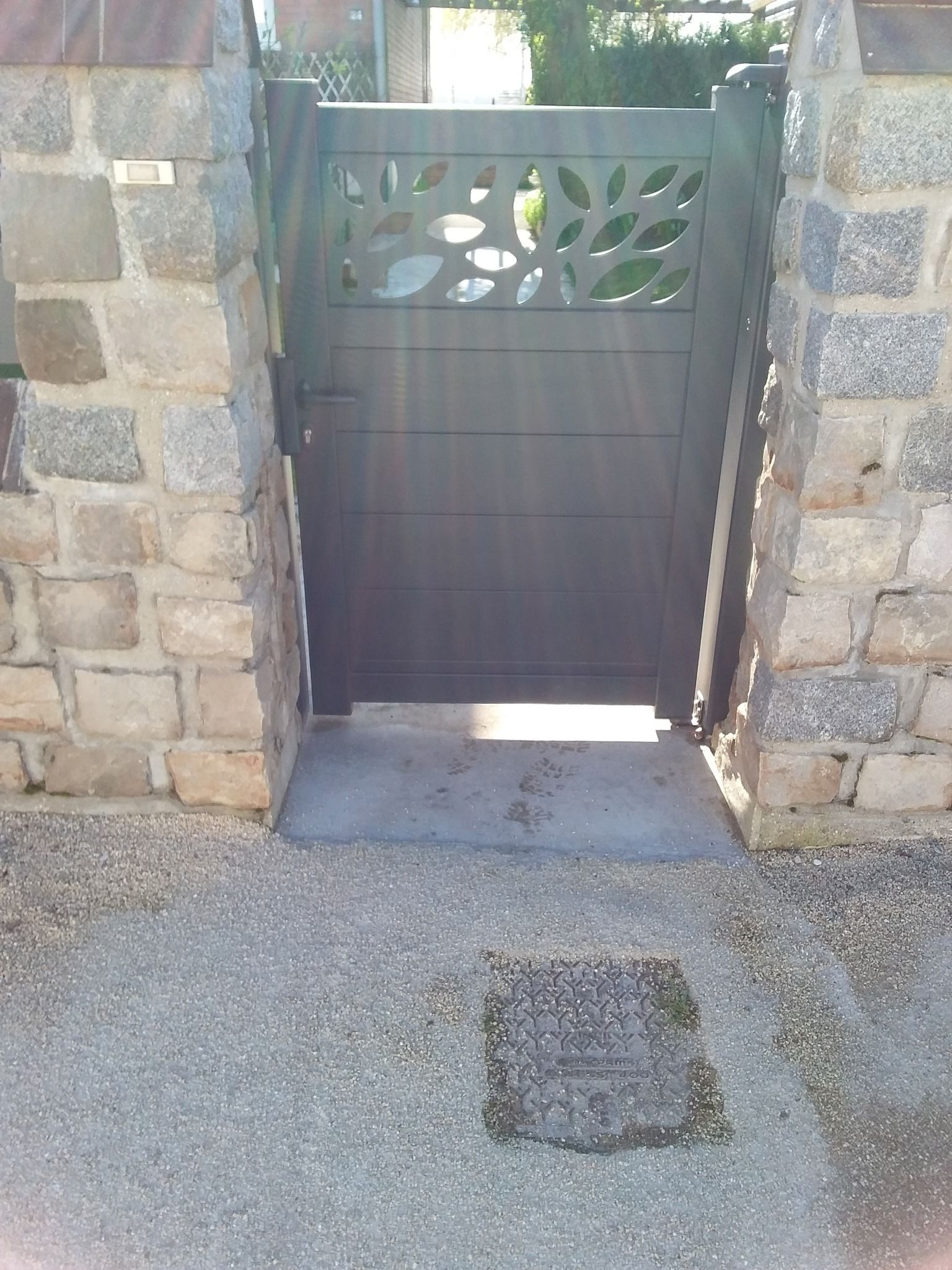 Un étroit portail noir, encadré par des murs de pierre, s'ouvre sur un chemin en béton.
