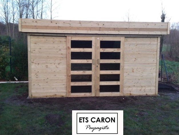 Petit hangar en bois avec double porte d'entrée et une pancarte indiquant ETS CARON au sol.