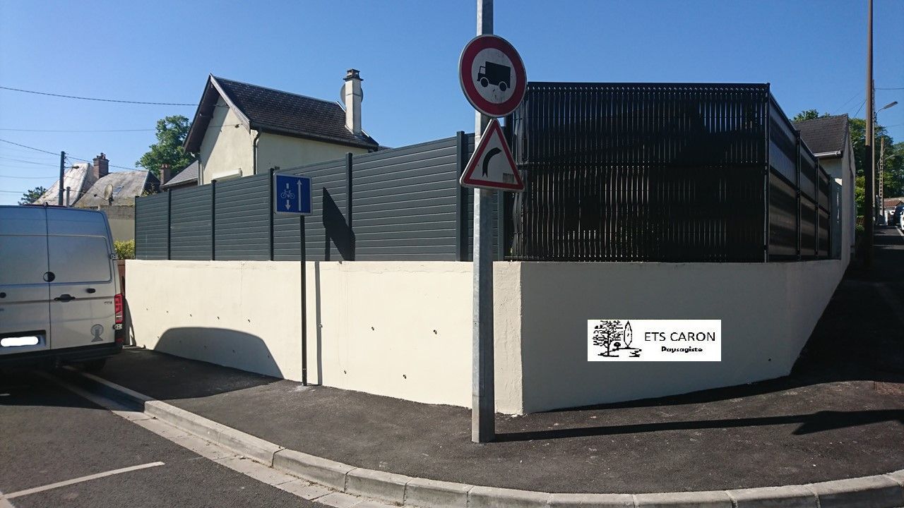 Un mur blanc et un portail noir à un coin de rue, avec une camionnette blanche garée.